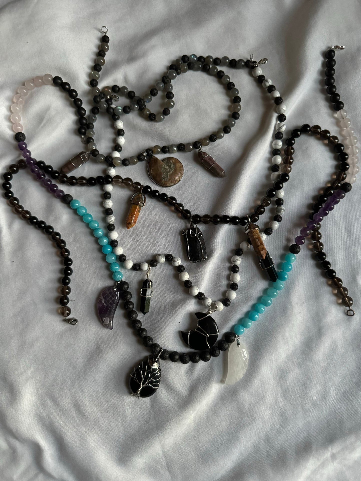 Multiple beaded necklaces with various beads and charms on a white fabric background