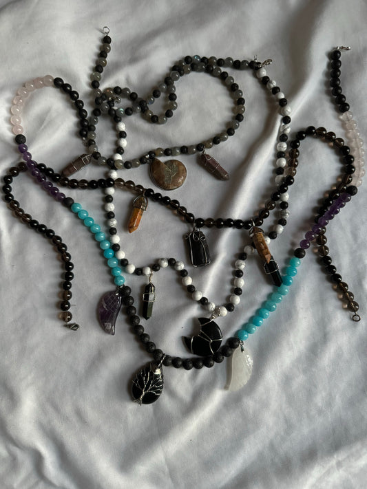 Multiple beaded necklaces with various beads and charms on a white fabric background