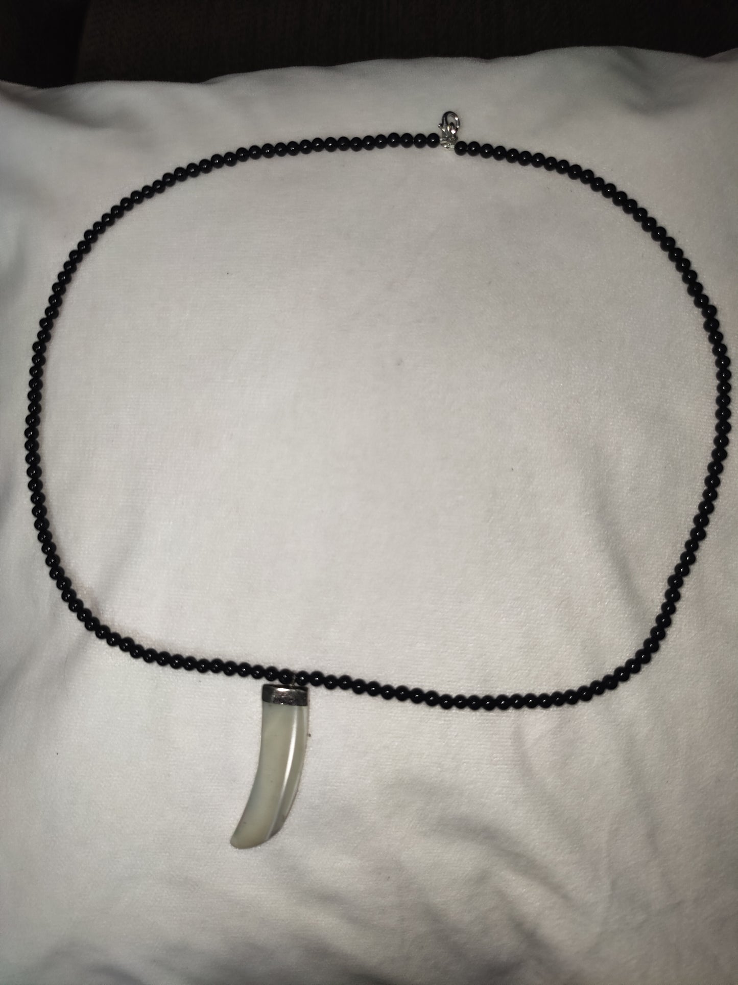 Necklace with a black beaded chain and silver pendant on a white surface