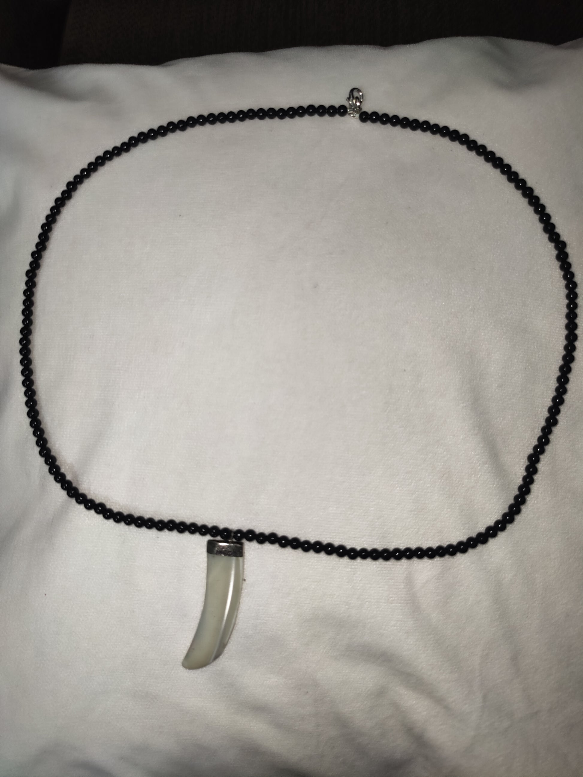 Necklace with a black beaded chain and silver pendant on a white surface